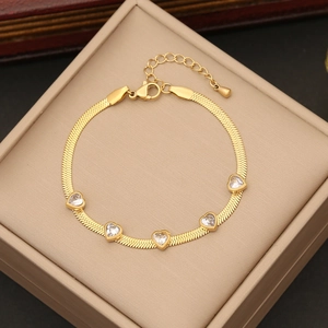 Golden blade chain bracelet with five heart-shaped gemstones on a beige jewelry box