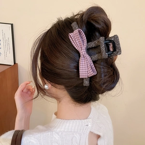 Detailed view of grey knit claw clip with pink checkered bow on model's hair