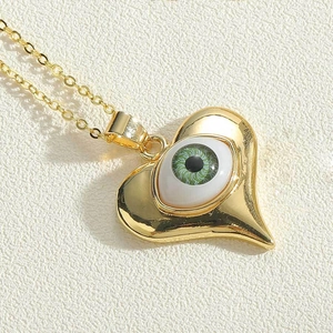 Macro view of gold heart pendant with green devil eye detail and delicate gold chain