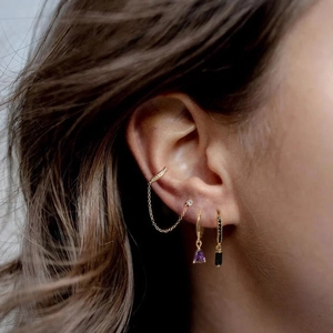 Dettaglio di orecchini a clip dorati con catena, pietre di zircone viola e nere