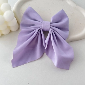 Detailed view of a large lavender purple satin bow hair clip on a minimalist white tray