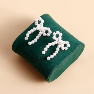 Detailed view of handmade bow earrings crafted from white pearls on green velvet