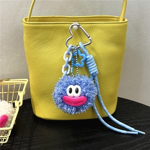 Detailed view of a blue plush monster charm with heart hook and cord on a yellow leather bag