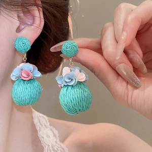 Detail of blue and pink woven flower earrings worn by a model in a close-up shot
