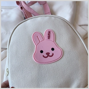 Close-up of white canvas toddler backpack with a cute pink rubber bunny patch detail