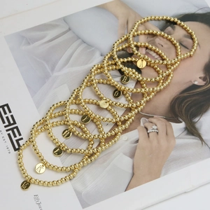 Close-up of golden beaded bracelets with personalized engraved alphabet letter charms