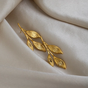 Detailed macro view of gold leaf earrings with delicate vein textures on beige fabric
