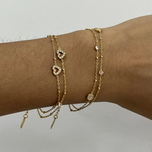 Dettaglio del bracciale a doppio strato dorato con strass a cuore e ciondolo a disco tondo