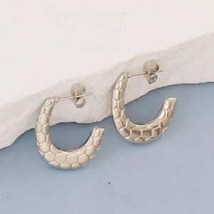 Macro shot of silver C-shaped earrings with geometric honeycomb texture on white stone base