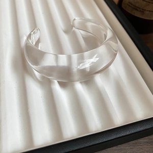 Close-up of a chunky transparent resin wave bangle on a white textured display tray