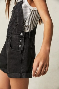 Detail view of washed black denim overalls showing side metal buttons and pocket texture