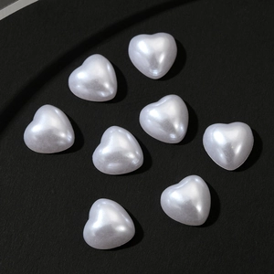 Macro shot of white heart-shaped faux pearl nail charms on a black background