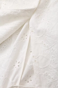 Close-up of white floral embroidery with delicate eyelet details on cotton fabric