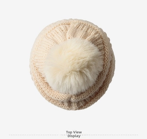 Vue de dessus d'un bonnet en maille beige avec détail de gros pompon en fourrure