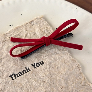 Detail of red suede bow hair clip on a minimalist white plate with a thank you card
