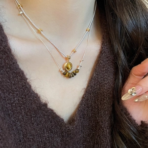 Close-up of layered tiger eye bead necklace with a gold-tone pendant on a brown sweater