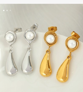 Close-up of teardrop earrings with white pearls in gold and silver finish on white tray