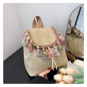 Close-up detail of a woven straw bucket bag featuring colorful tassels and drawstring closure