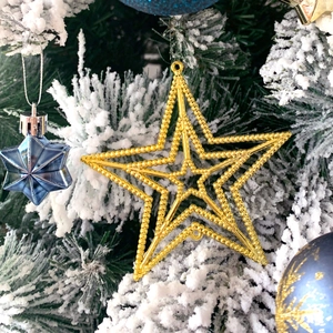 Detailed close-up of golden beaded star and blue faceted ornaments on snowy pine branches