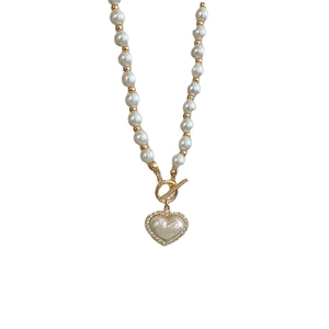Elegante Perlenkette mit goldenen Perlen und glitzerndem Herzanhänger auf weißem Grund