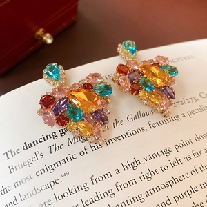 Macro shot of colorful zirconia heart earrings with mixed gems on a vintage paper background