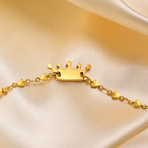 Detail of a golden stainless steel crown bracelet with heart-shaped links on silk