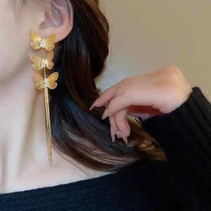 Close-up of elegant gold tassel earrings with zircon butterflies on a female model