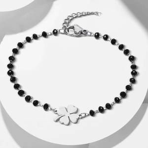 Detail view of black beaded bracelet featuring silver clover charm and lobster clasp closure
