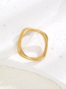Detail of a modern gold-plated irregular wavy ring placed on a textured white stone base