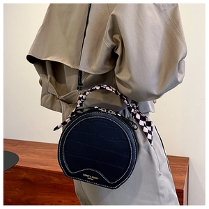 Detail of black round crocodile pattern bag with silk scarf and gold chain strap