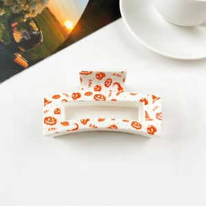 Close-up of white square hair claw clip with orange Halloween skull and pumpkin patterns