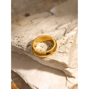 Close-up of a wide 18k gold-plated stainless steel ring on a textured stone base