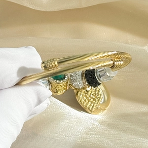Detail of gold charm bracelet featuring green gemstone heart and pave crystal pendants