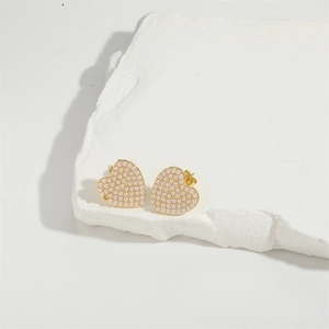 Detail shot of heart-shaped earrings with faux pearls and gold plating on white stone