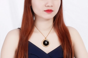 Close-up of model wearing gold necklace with a round black resin pendant and gear frame