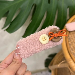 Detailed view of a pink plush hair clip featuring a cute button and orange bow detail