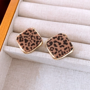 Close-up of leopard print diamond earrings with gold trim on a soft velvet tray