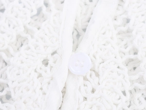 Detailed macro view of a white button on hollow-out crochet knit fabric blouse