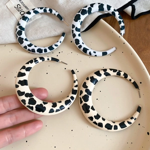 Close-up of large C-shaped hoop earrings with black and white cow print resin finish