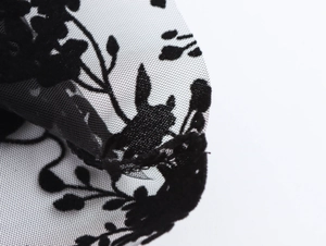Close-up of black floral lace fabric texture with intricate mesh detailing on the shirt