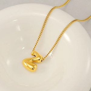 Close-up of golden bubble S letter pendant on a fine titanium steel curb chain