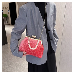 Detail of red velvet shell bag with pearl handle and gold frame worn as a crossbody