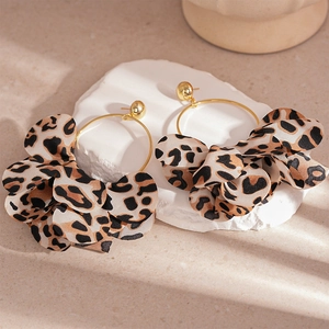 Detail of leopard print fabric petals on golden hoop earrings over a minimalist stone base