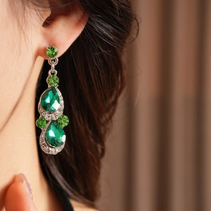 Close-up of vintage teardrop earrings with green crystals and silver metal on model
