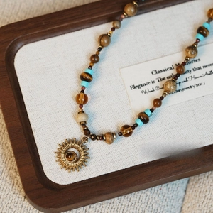 Vue détaillée d'un collier de perles vintage avec pendentif soleil doré et œil de tigre