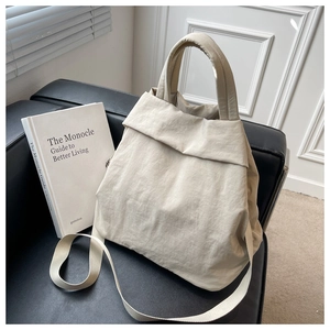 Detailed texture of off-white nylon tote bag placed on a black leather sofa with magazine