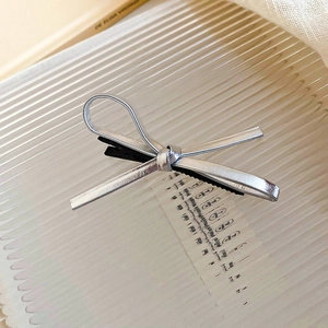 Macro detail of silver faux leather bow hair clip with metallic finish on glass tray