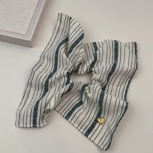 Détail d'un chouchou en tissu rayé beige avec un pendentif coeur doré poli et gravé