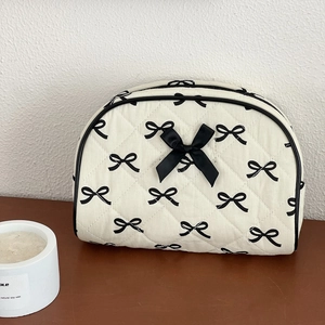 Detail of white quilted toiletry bag with black bow print and 3D ribbon on wood surface