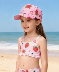 Ensemble maillot de bain enfant rose à motif fraise avec chapeau sur plage ensoleillée
